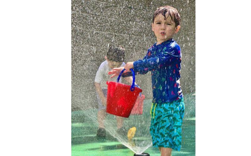Preschooler playing with bucket in a sprinkler